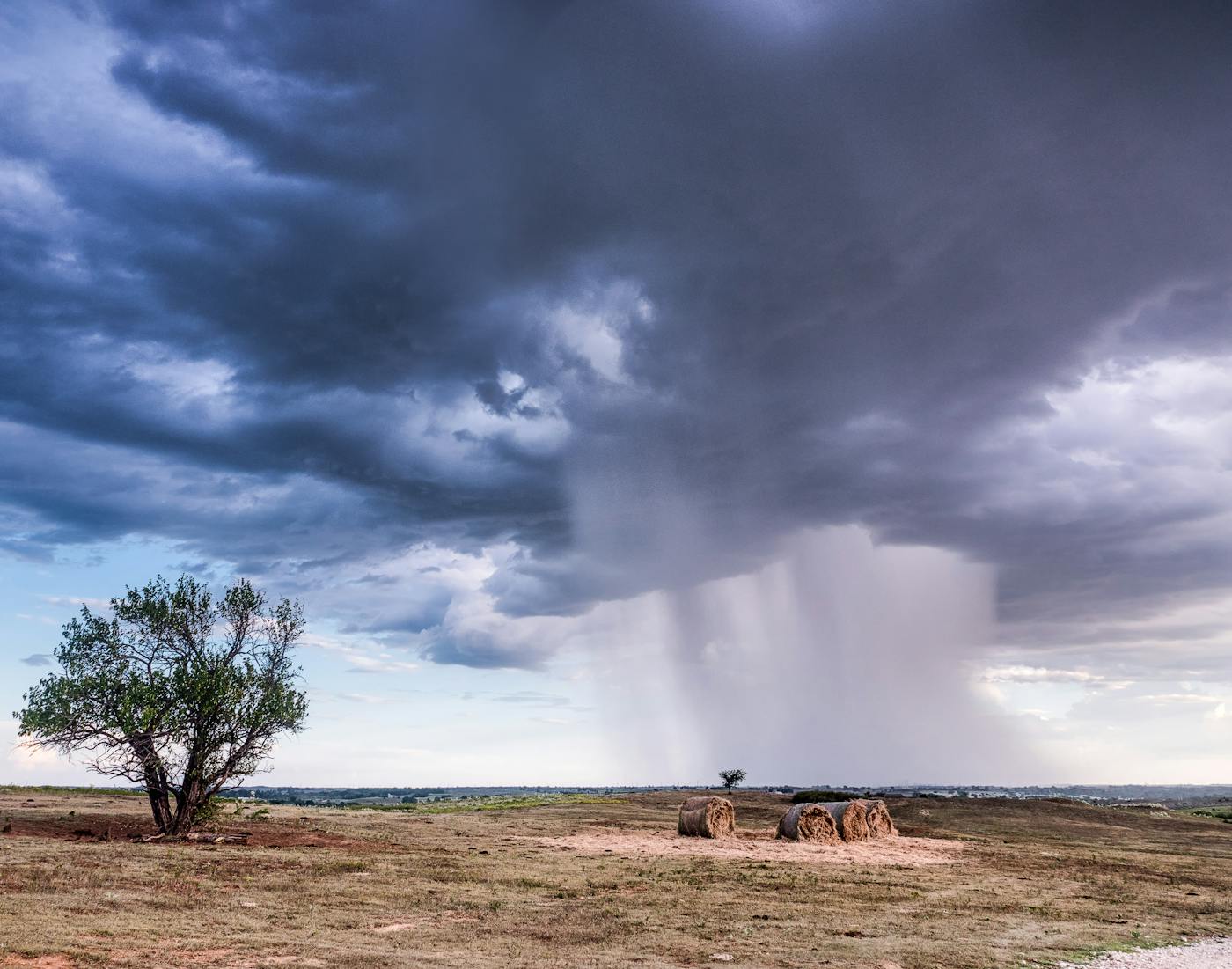 A lone tree and hay bales on the open Oklahoma prairie under a summer storm